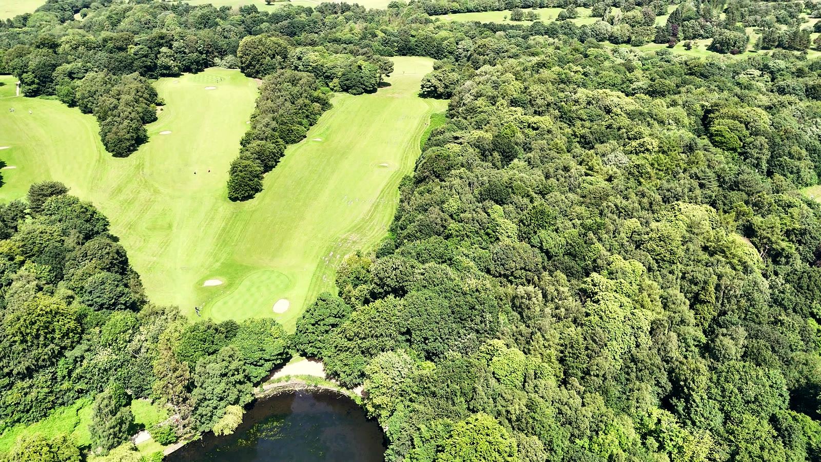 The seventh fairway from the air, tree-lined, bending right toward the green